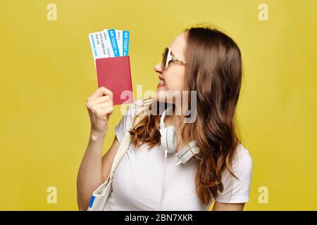 Une fille caucasienne en lunettes regarde un passeport avec des billets d'avion sur fond jaune comme un concept de vacances. Gros plan. Banque D'Images