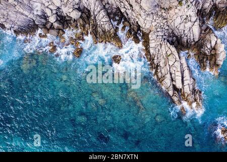 vue aérienne de dessus de l'océan turquoise clair avec des vagues de mer frapper et s'écraser sur les falaises du bord de mer de la côte rocheuse avec pulvérisation et mousse, pow Banque D'Images