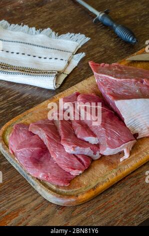 Tranches de bœuf cru sur une planche à découper en bois. Un grand morceau de filet de bœuf frais et cinq fines tranches de viande. Le processus de préparation de la viande de dishe Banque D'Images
