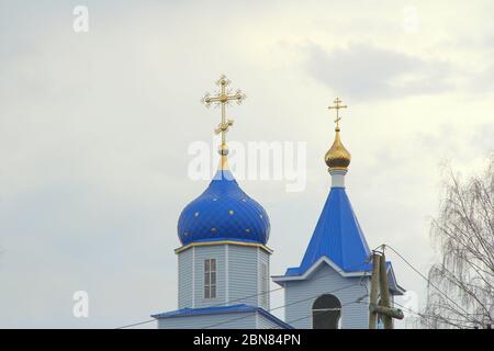 Église chrétienne orthodoxe avec murs blancs, dômes bleus et croix d'or en Russie. Un bâtiment pour les cérémonies religieuses avec un clocher contre un ciel nuageux dans la campagne. Banque D'Images