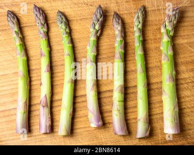 Sept épis d'asperges alignés sur une planche à découper en bois Banque D'Images