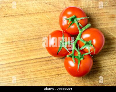 Quatre tomates rouges mûres sur la vigne sur une planche à découper en bois avec espace pour copier Banque D'Images