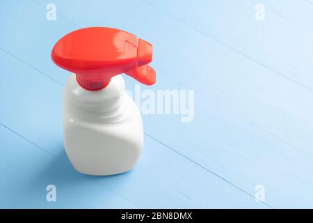 Bouteille de spray nettoyant avec un boîtier blanc sans inscriptions et un distributeur rouge vif sur fond en bois bleu clair. Fermeture des produits de lavage à domicile- Banque D'Images