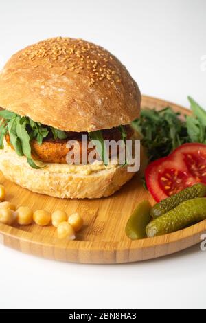 Hamburger de houmous de falafel vegan avec pain de levain maison, tomates, concombres marinés et arugula dans une assiette en bois Banque D'Images