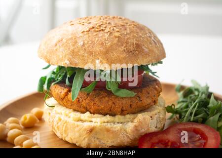 Hamburger de houmous de falafel vegan avec pain de levain maison, tomates, concombres marinés et arugula dans une assiette en bois Banque D'Images