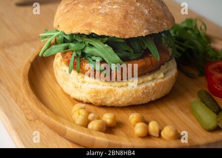 Hamburger de houmous de falafel vegan avec pain de levain maison, tomates, concombres marinés et arugula dans une assiette en bois Banque D'Images