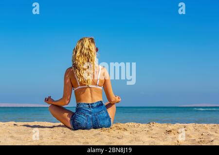 Jeune femme blanche blonde aux cheveux longs médite sur la plage égyptienne Banque D'Images