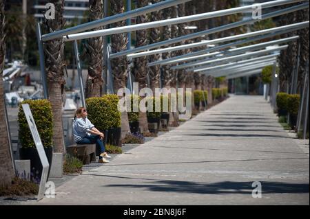 Malaga, Espagne. 13 mai 2020. Une femme se reposant sur un banc le long de la voie de randonnée vide de 'Muelle Uno' pendant le verrouillage partiel après le début de la phase 1 dans certaines villes.l'Espagne passe par le plan de réduction vers une ''nouvelle normalité' en assouplissant les mesures qui ont résulté de l'épidémie de COVID-19, des villes comme Madrid, Barcelone, Malaga ou Grenade continuent dans la phase 0 en raison des avis épidémiologiques des autorités sanitaires. Crédit: Jesus Merida/SOPA Images/ZUMA Wire/Alay Live News Banque D'Images