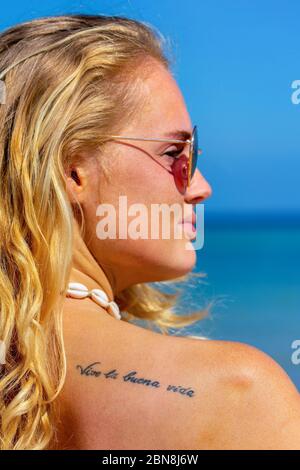 Portrait de jeune femme blonde avec tatouage 'vivre la bonne vie' en espagnol sur l'épaule Banque D'Images