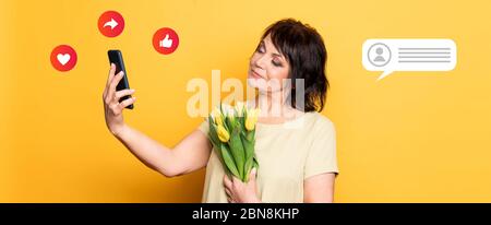 Belle vieille femme avec maquillage professionnel fumé et coiffure tenant des fleurs de tulipe sur le fond rose. Prise d'un appel vidéo par le smartphone Banque D'Images