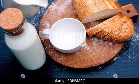 Gros plan sur le versement de lait dans une tasse blanche sur fond de bois à côté du pain. Banque D'Images