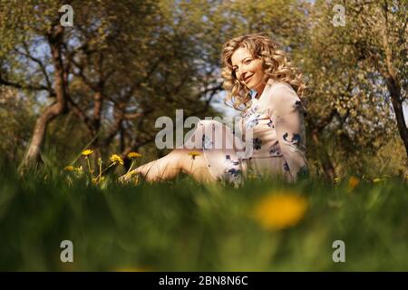 Une femme adorable se repose dans le parc d'été verdoyant avec des pissenlits Banque D'Images