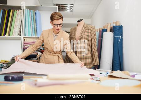 Jeune tailleur de lunettes debout près de son lieu de travail et de mettre le tissu sur la table qu'elle va faire une robe Banque D'Images