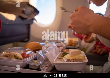 un avion passager en gros plan mange un délicieux repas chaud à bord sur une table pliante. en arrière-plan, il y a une fenêtre dans le hublot. Banque D'Images