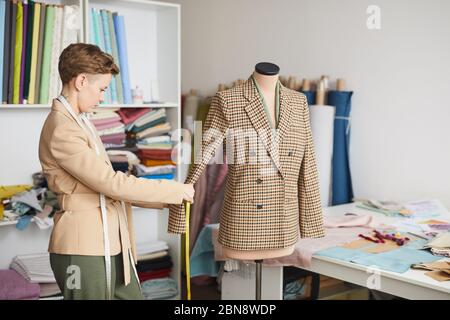 Jeune couturier prenant des mesures de la veste avec mètre ruban dans l'atelier Banque D'Images