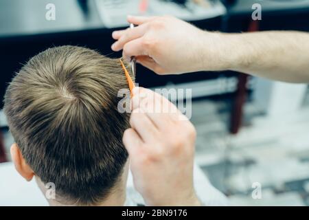 Le coiffeur tatoué coupe les cheveux du client avec des ciseaux. Gros plan. Un homme attrayant obtient une coupe de cheveux moderne dans le salon de coiffure. Vue rapprochée. Banque D'Images
