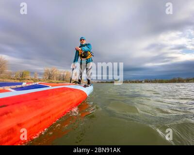 Vue en contre-plongée depuis la caméra embarquée d'un pagayeur senior sur un long stand de course en haut de paddleboard sur un lac dans le Colorado. Loisirs, formation et de la fitn Banque D'Images