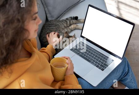 Jeune fille hispanique se relaxant sur un canapé avec chat regardant l'écran de mockup portable. Banque D'Images