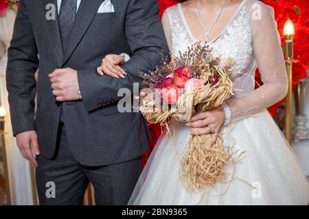 La mariée est entrée dans l'aisselle du marié et a tenu un bouquet de fleurs . corail séché atteindre le blé rose coton fleur bouquet de mariée . Banque D'Images