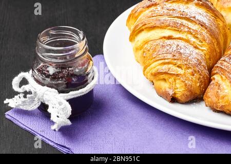 Croissants français en gros plan, jarre de confiture servie sur une serveuse pourpre. Cuisson maison à base de pâte feuilletée. Banque D'Images