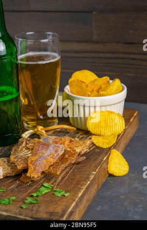 Morue séchée au poivre avec bière, citron et chips de pomme de terre sur un panneau en bois sombre. En-cas sur le poisson avec de la bière. Gros plan Banque D'Images