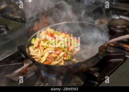 Chef cuisinez avec feu dans une poêle. Chef professionnel dans une cuisine commerciale de style flambe. Cuisiniers friture des aliments dans une poêle à frire sur une table de cuisson à gaz en co Banque D'Images