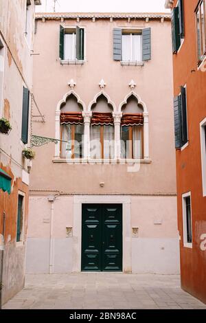 Façade d'une maison de pêche de trois étages à Venise, Italie. Porte avant en bois vert massif, trois fenêtres vénitiennes classiques avec un haut pointu, des colonnes et Banque D'Images