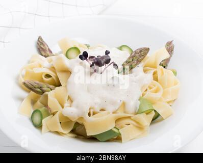 Plat de pâtes maison frais de fettuccine ou tagliatelle, asperges vertes, sauce blanche, dans une assiette blanche sur table en bois blanche Banque D'Images