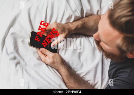 Fausses nouvelles infodemics pendant le concept de pandémie de Covid-19. Les mains de l'homme tenant le téléphone mobile lire les nouvelles mondiales ou le réseau social à la maison. Lire la dernière actualité Banque D'Images