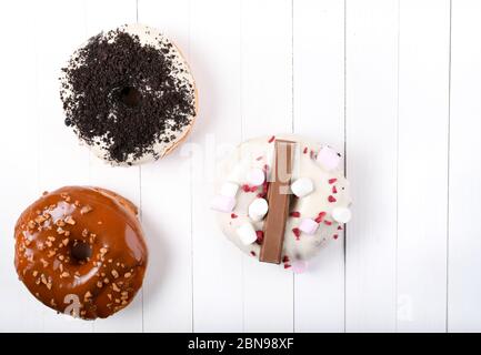 Trois fondus émaillés de chocolat noir et blanc, marshmallows, biscuit crumbles, beignets enrobés de sucre caramel sur bois blanc Banque D'Images