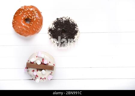 Trois fondus émaillés de chocolat noir et blanc, marshmallows, biscuit crumbles, beignets enrobés de sucre caramel sur bois blanc Banque D'Images