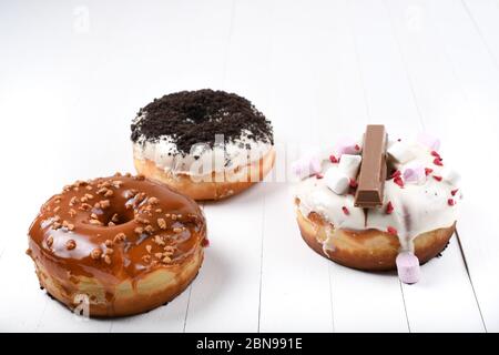 Trois fondus émaillés de chocolat noir et blanc, marshmallows, biscuit crumbles, beignets enrobés de sucre caramel sur bois blanc Banque D'Images