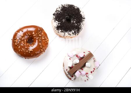 Trois fondus émaillés de chocolat noir et blanc, marshmallows, biscuit crumbles, beignets enrobés de sucre caramel sur bois blanc Banque D'Images