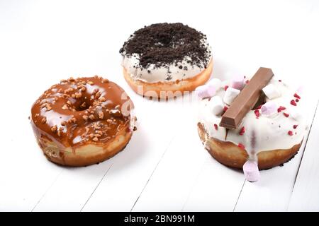 Trois fondus émaillés de chocolat noir et blanc, marshmallows, biscuit crumbles, beignets enrobés de sucre caramel sur bois blanc Banque D'Images