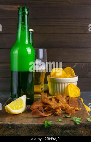 Calmar péruvien avec bière, citron et chips de pomme de terre sur un panneau en bois sombre. En-cas sur le poisson avec de la bière. Gros plan Banque D'Images