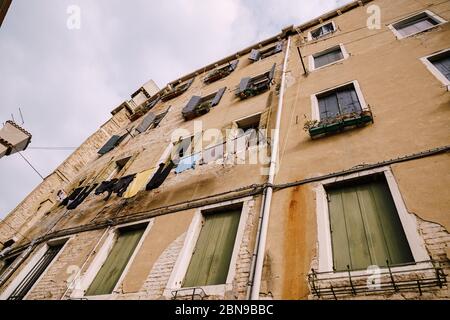 Cadre large par dessous sur une façade de bâtiment en Italie, Venise. Le bâtiment de quatre étages est de couleur sable et est doté de fenêtres avec volets en bois et pots de fleurs Banque D'Images