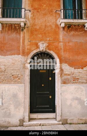 Gros plans des façades de bâtiments à Venise, Italie. Une porte noire en bois dans une porte voûtée avec une grille métallique sur le dessus, dans la façade d'une brique orange Banque D'Images