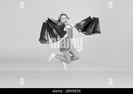 Hurry up. Acheter plus rapidement. Happy girl jump with shopping bags. Petit enfant sourire avec des sacs en papier. Préparation et célébration des fêtes. Shopping sur le black friday. Shopping d'inspiration. Traiter avec succès. Banque D'Images