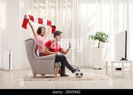 Un jeune homme et une jeune femme regardent un match de football à la télévision à la maison et applaudissent Banque D'Images