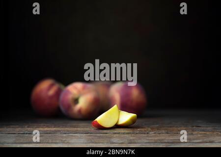 Nectarines fraîches, entières et coupées en tranches, sur une table rustique en bois avec un fond sombre Banque D'Images