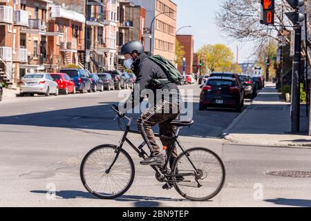 Montréal, CA - 13 mai 2020 : un homme avec un masque facial à vélo pendant la pandémie du coronavirus COVID-19. Banque D'Images