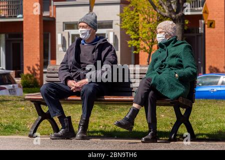Montréal, CA - 13 mai 2020 : homme et femme âgés avec masque facial sur un banc dans un parc, pendant la pandémie Covid-19 Banque D'Images