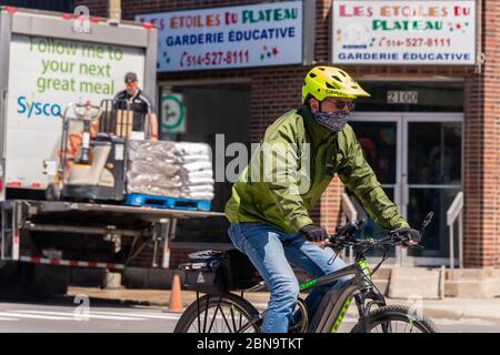 Montréal, CA - 13 mai 2020 : un homme avec un masque facial à vélo pendant la pandémie du coronavirus COVID-19. Banque D'Images