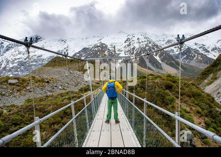 Le randonneur traverse un pont suspendu au-dessus de la rivière Hooker, de la vallée Hooker, du parc national Mount Cook, de Canterbury, de Nouvelle-Zélande, d'Océanie Banque D'Images