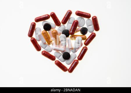 Divers comprimés blancs et noirs posent un coeur, médicament de coeur, sur un fond blanc, des capsules, des pilules et des dragées Banque D'Images