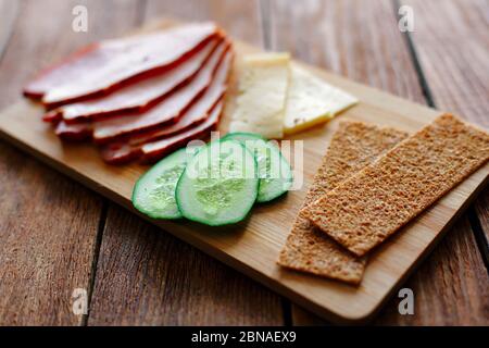 Trancher du jambon, des concombres et du fromage avec des pains fins et grossiers se trouvent sur une planche en bois. Banque D'Images