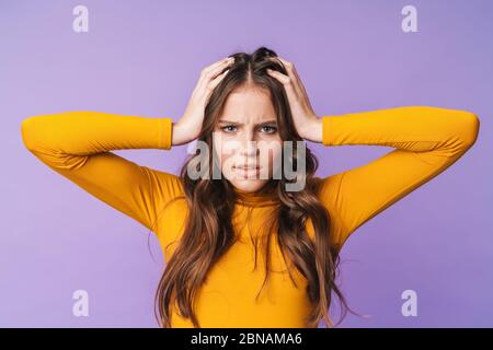 Image de jeune femme mécontente avec de longs cheveux bruns nerveux et saisissant sa tête isolée sur fond violet Banque D'Images