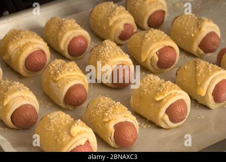 Les saucisses crues dans la pâte avec le sésame sur une plaque à pâtisserie sont prêtes à cuire. Gros plan. Cuisiner à la maison. Banque D'Images