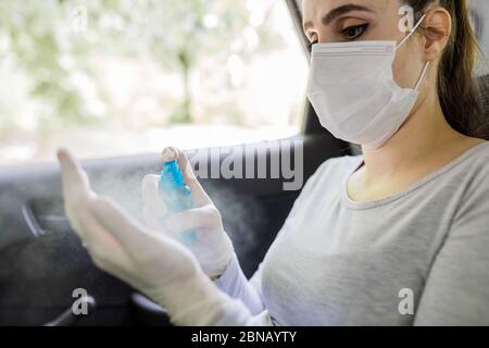 Femme avec masque chirurgical portant des gants médicaux et utilisant les mains pulvérisateur antiseptique tout en étant assis sur le siège arrière de voiture, concept de prévention des coronavirus. Banque D'Images