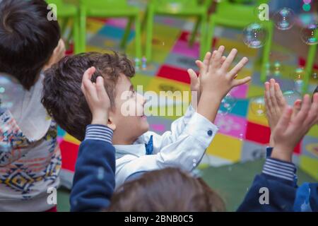 Joli petit garçon attrapant des bulles de savon . Petit garçon blond jouant avec des bulles de savon . Enfants à la fête. Des bulles de savon apparaissent. Fête d'enfants. À Banque D'Images